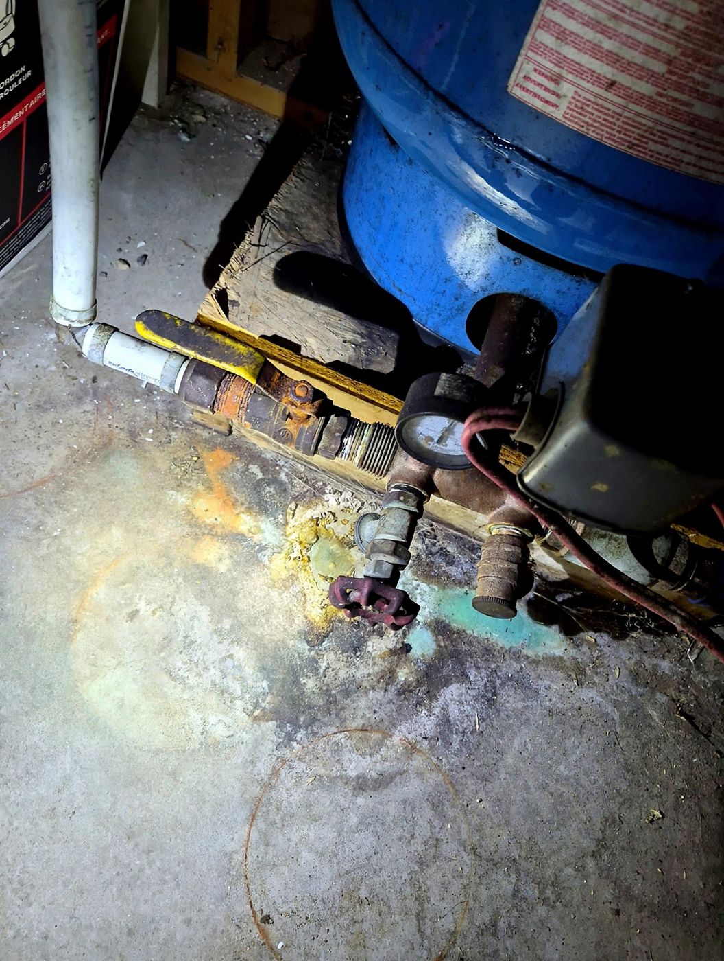 Réservoir de pression d'un puits : valves rouillées et traces de fuite au sol.