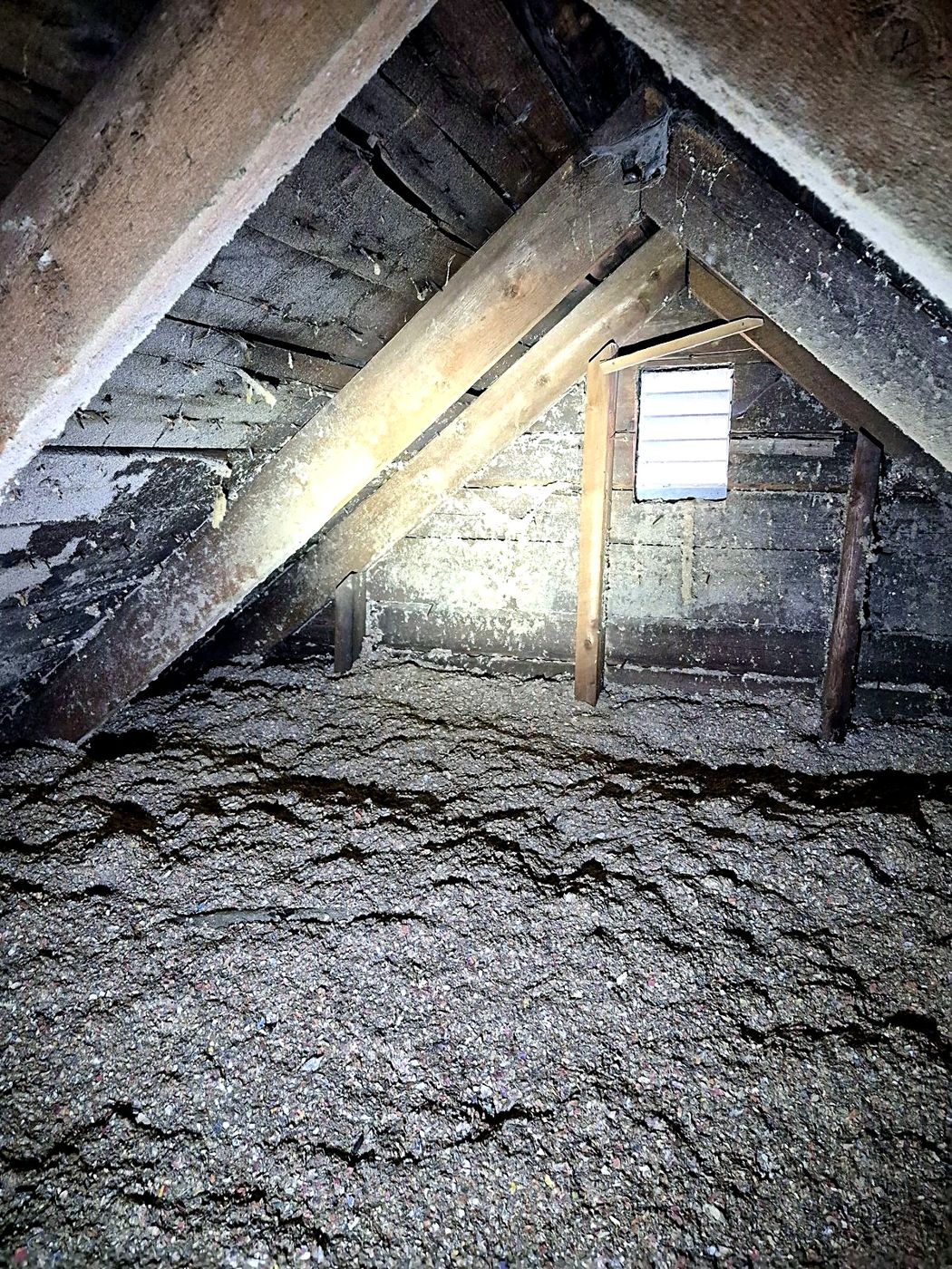 Entretoit d'une vieille maison : chevrons de bois et isolant soufflé.