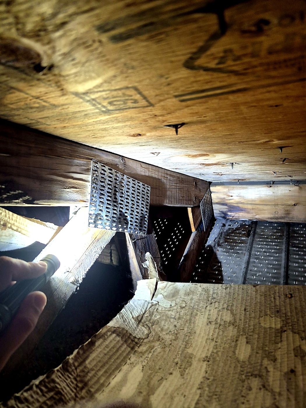 Contreplaqué de toiture taché et détérioré par l'humidité, vu de l'entretoit — l'eau s'infiltre quelque part.